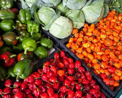 A vibrant display of fresh vegetables including peppers and cabbage at an outdoor market.